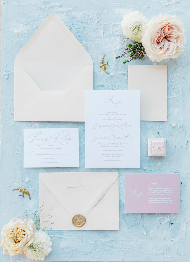 blush pink calligraphy invitation on blue background with blush roses