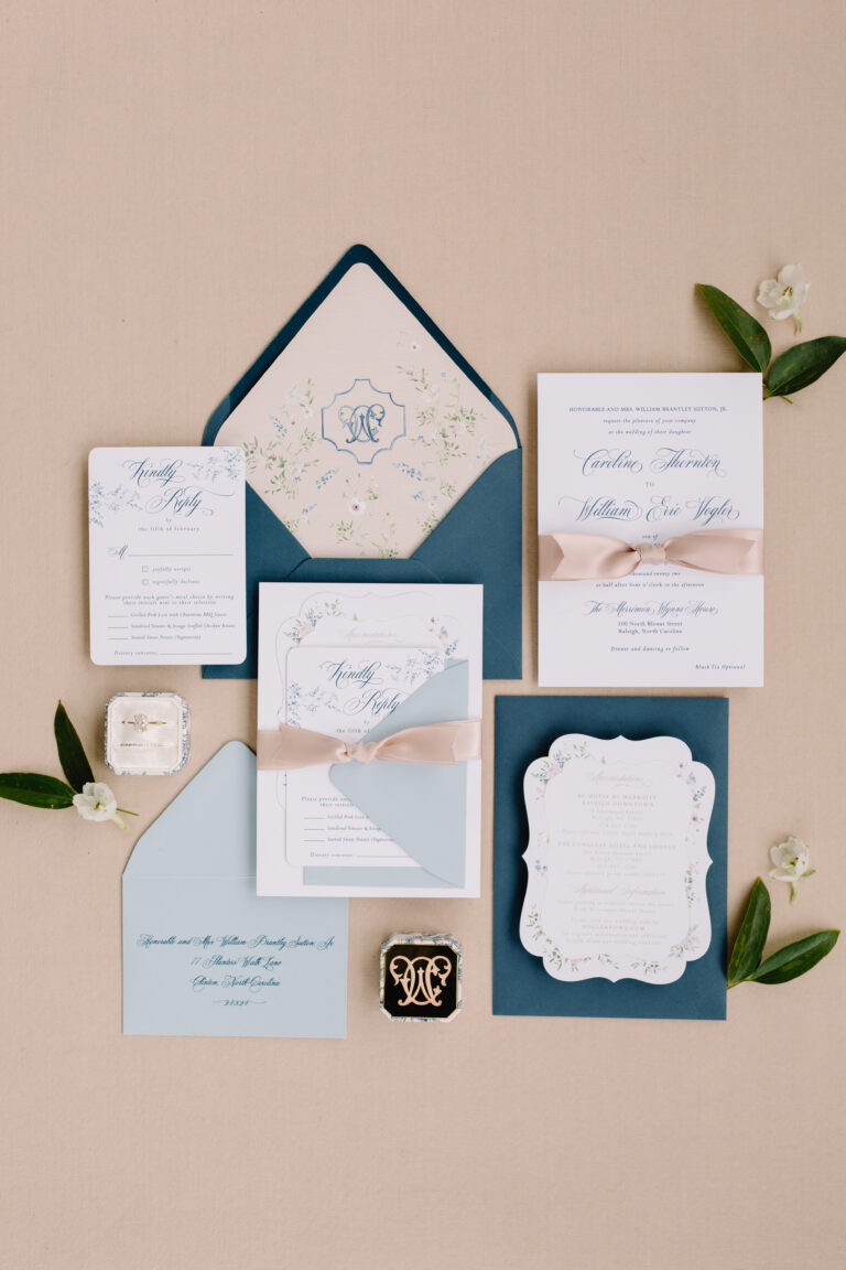 blue and white ginger jar inspired wedding invitations on a tan background with champagne ribbon and blue envelopes