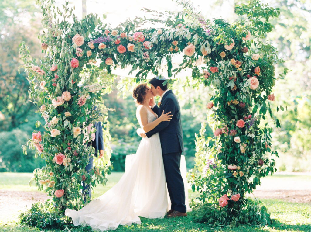couple kissing under floral arch at their ceremony