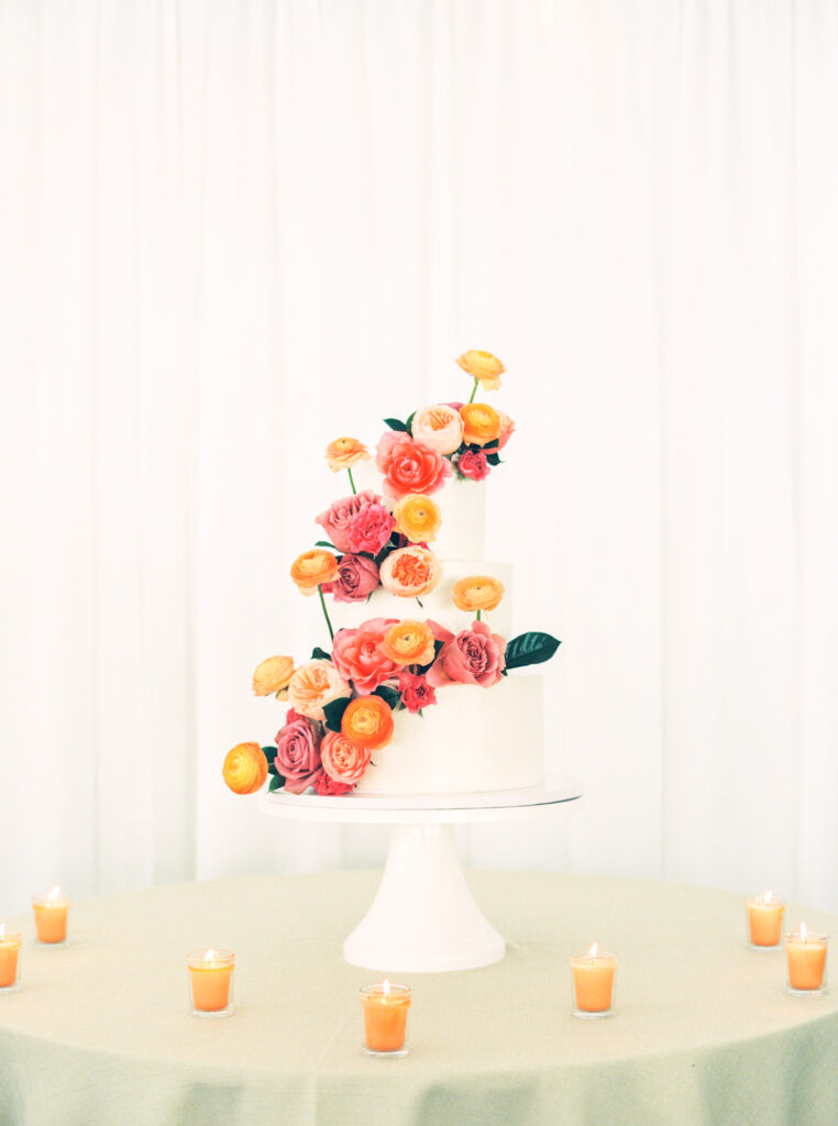white wedding cake with color blooms or orange and pink
