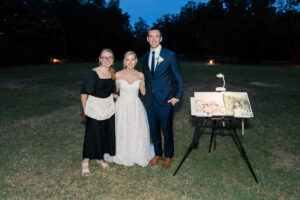 a newlywed couple pose with live wedding painter and finished painting from wedding ceremony and wedding bouquet