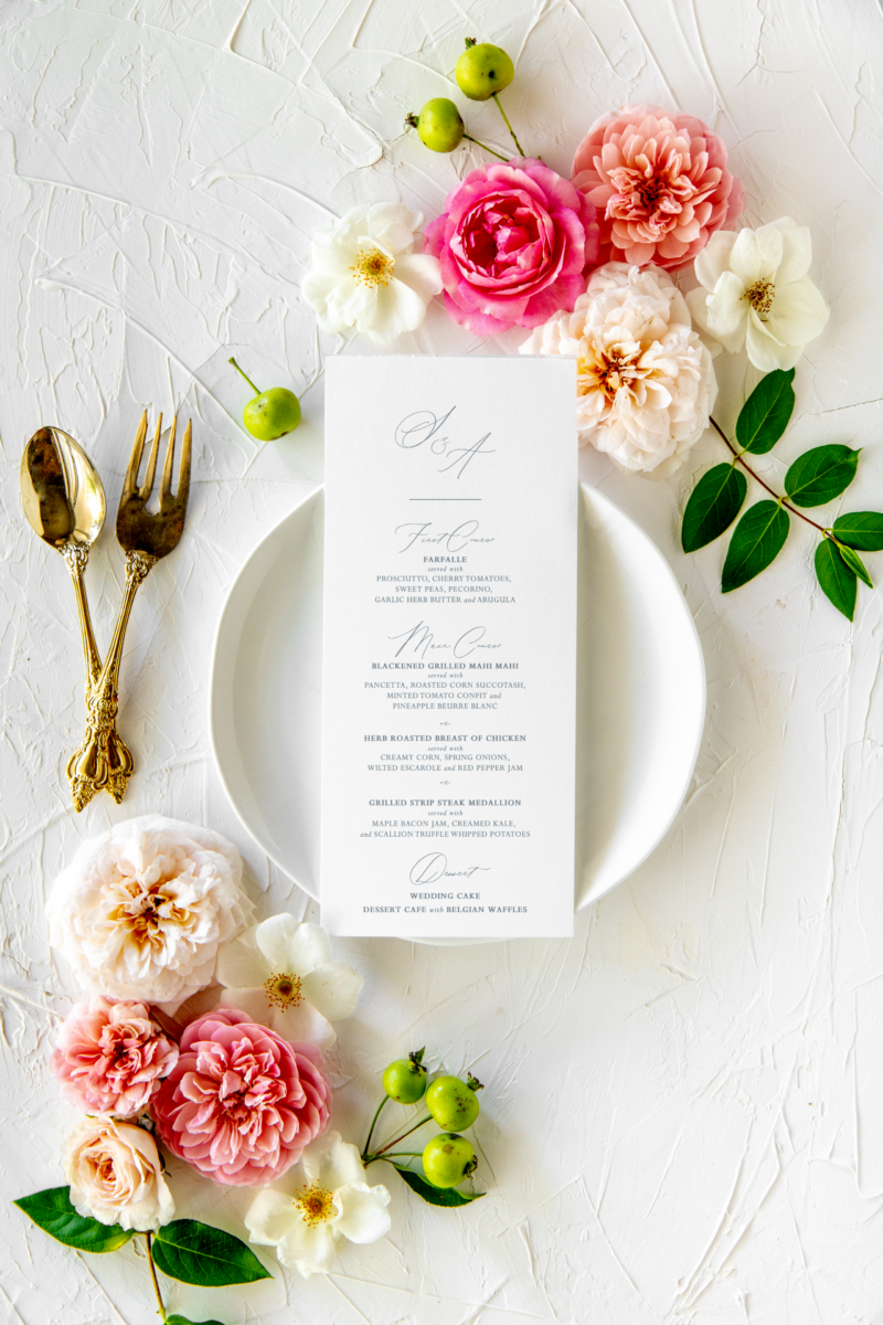 White dinner menu on floral tables cape with couple's initials at the top in blue font