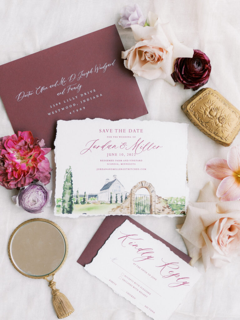 Redeemed Farms and Vineyards watercolor painting as a save the date on a rose filled background with burgundy envelopes and antique charms as a flatlay image