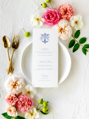 White dinner menu on floral tables cape with couple's monogram at the top in blue font