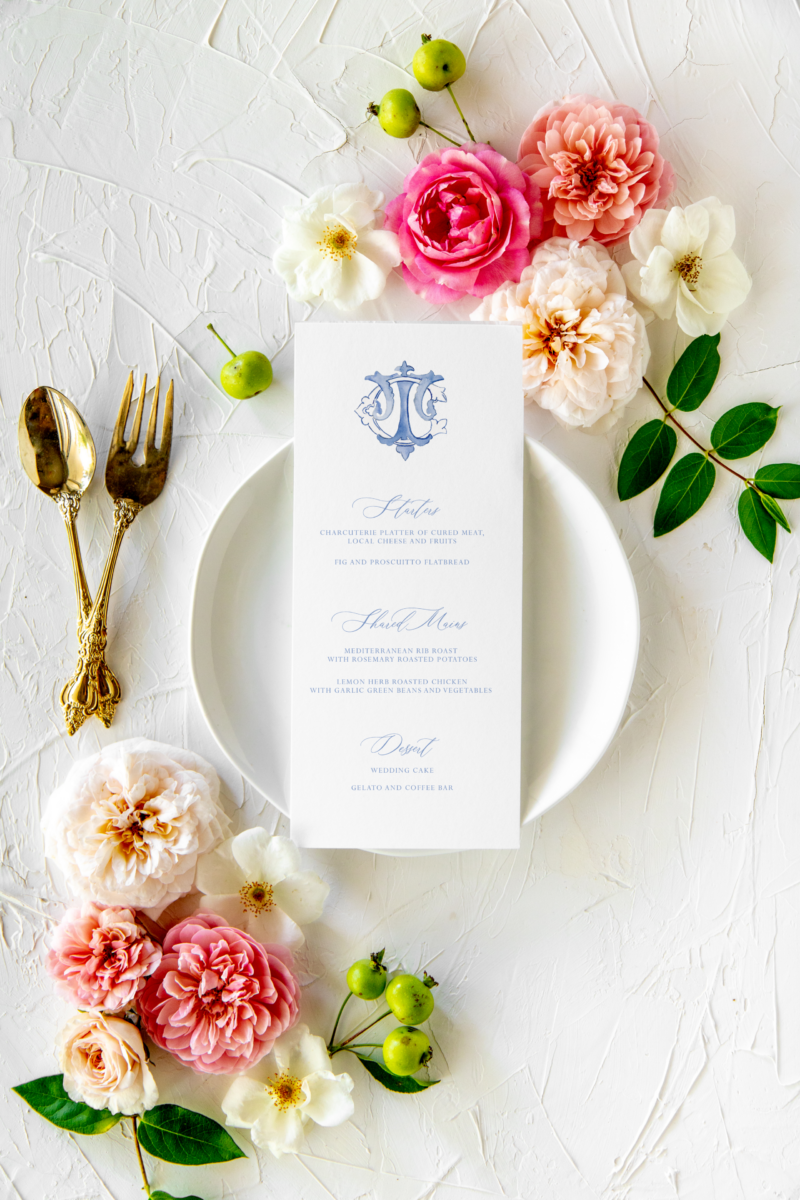 White dinner menu on floral tables cape with couple's monogram at the top in blue font
