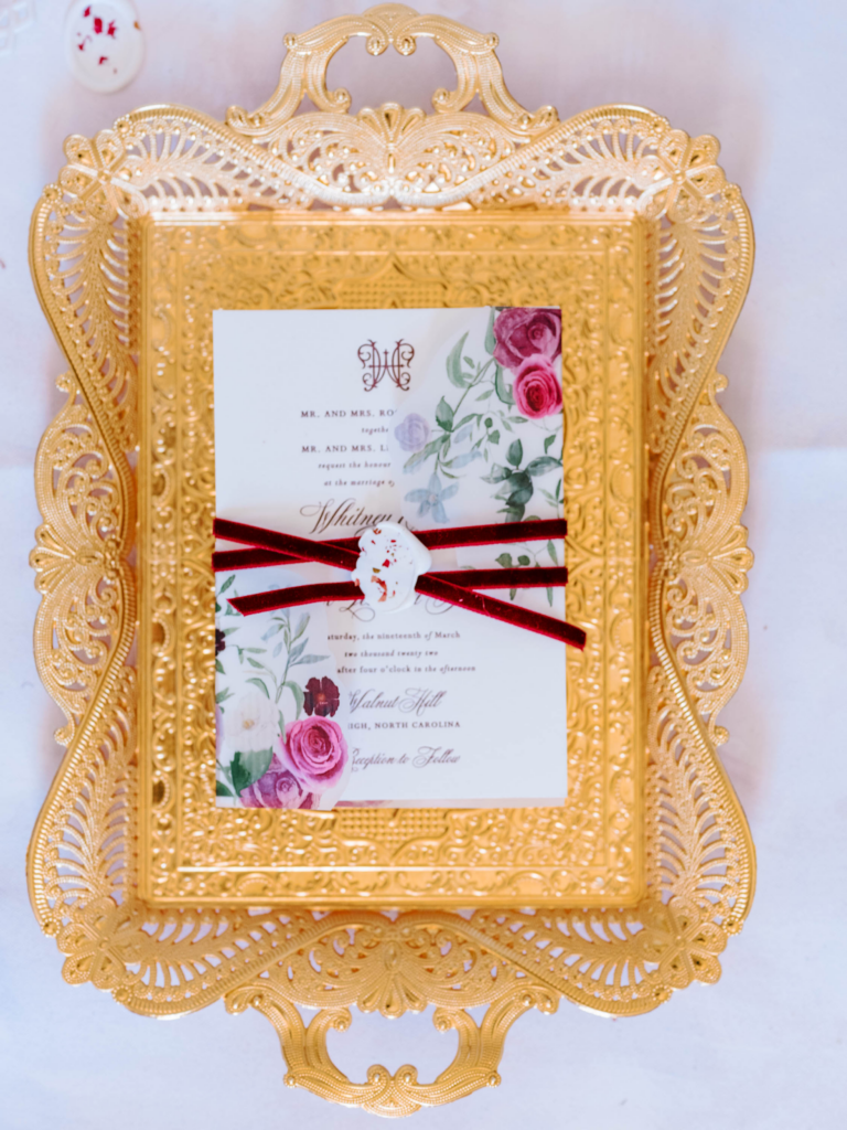 white and magenta wedding invitation on gold tray
