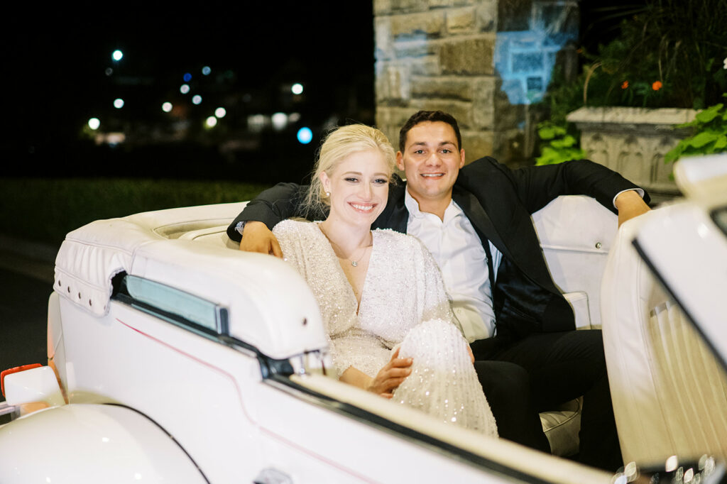 bride and groom pose for getaway in classic car after their reception