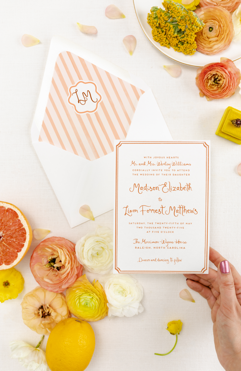 orange and white stripe custom wedding invitation on a white background with grapefruit and ranunculus in the corners