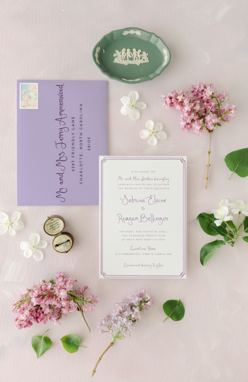 lilac whimsical wedding invitation on a light purple background with lilac flowers