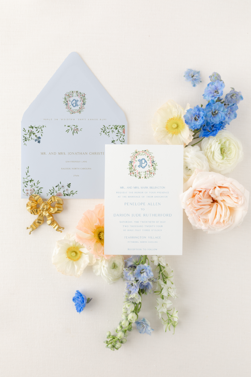 pastel spring flowers and greenery on a white background with pastel wedding invitation and blue envelope